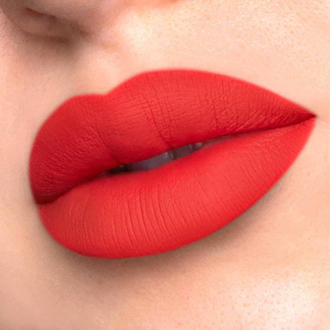 Divine a deep rich coral liquid lipstick swatched on model.