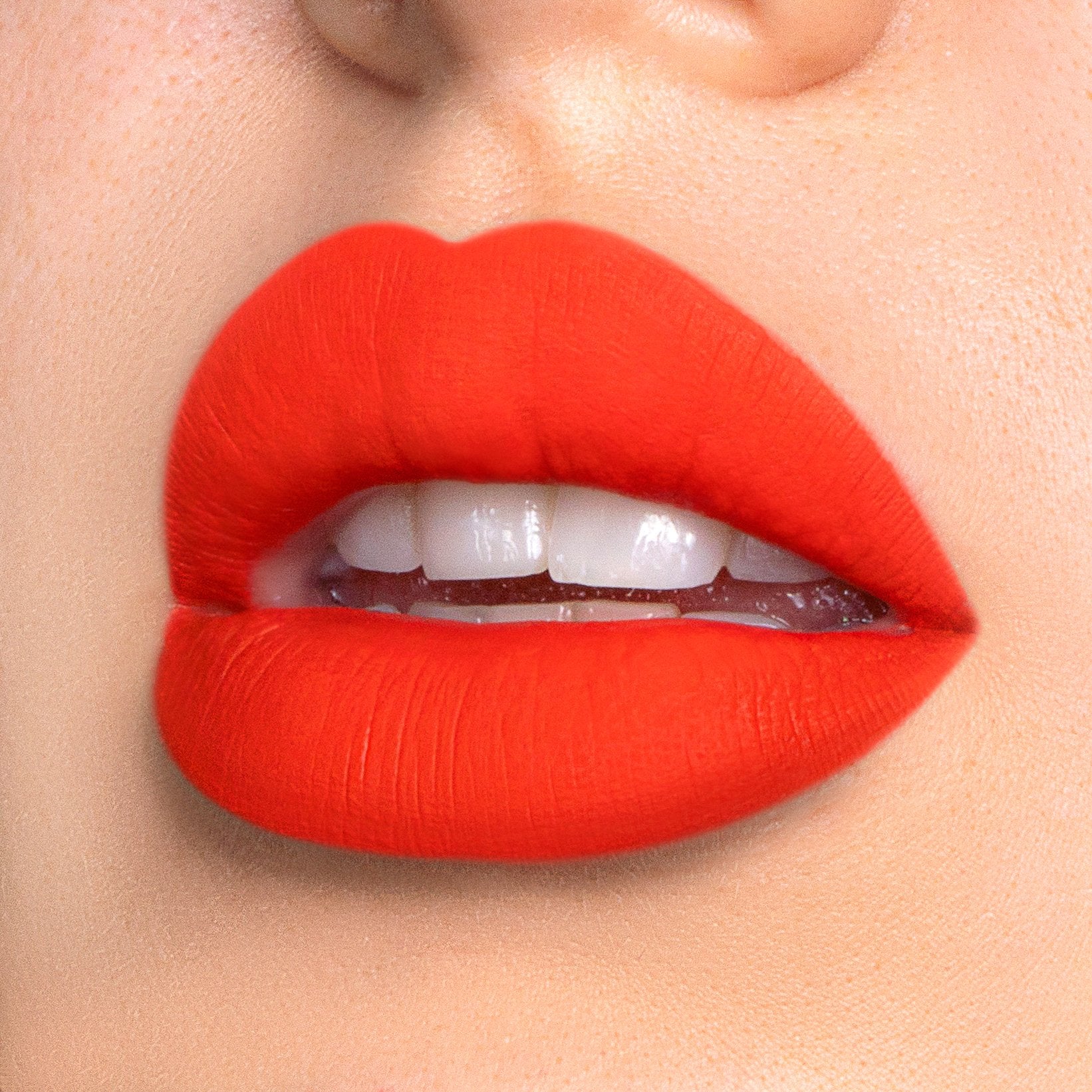 Flirt a bright orange liquid lipstick swatched on model
